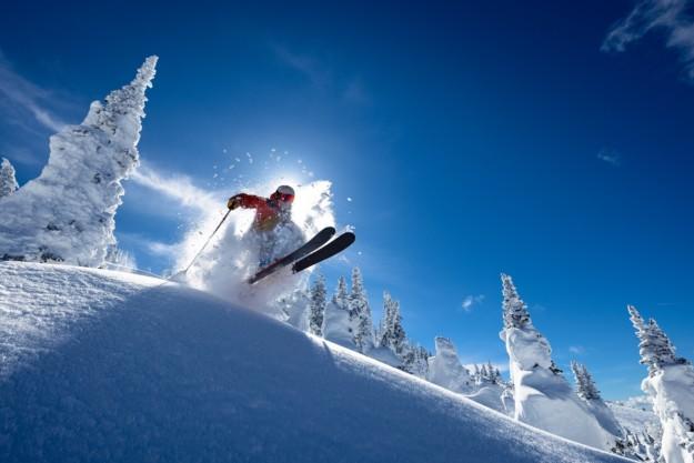 a skier in an orange jacket launches over a lip