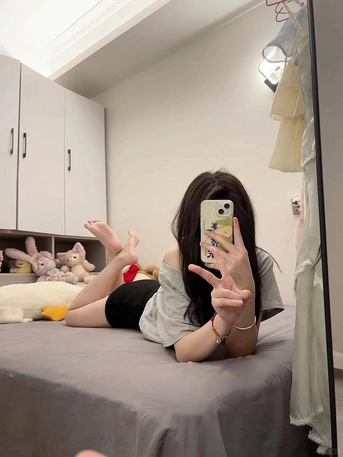 Một cô gái trẻ xinh đẹp đang tạo dáng che mặt bằng điện thoại trong phòng với ánh sáng tự nhiên nhẹ nhàng