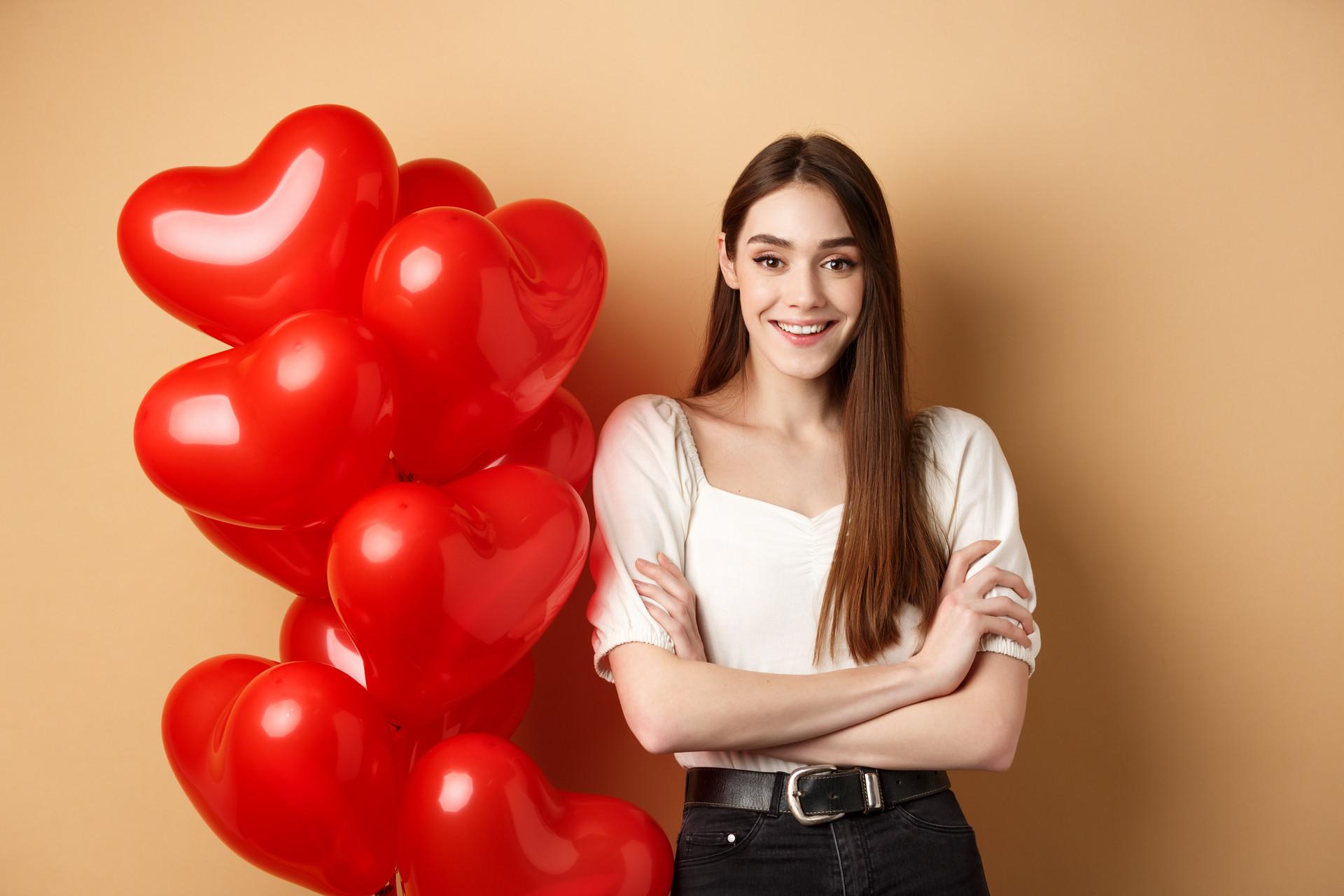 cheerful young woman looking happy valentines day standing near hearts balloons with arms crossed.jpg